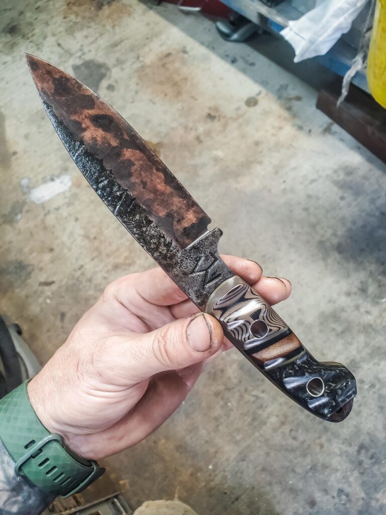 Apocalyptic finish 80crv2 Bushcraft with carbon fiber and G10 handle with a dark brown Micarta split and titanium pins.
