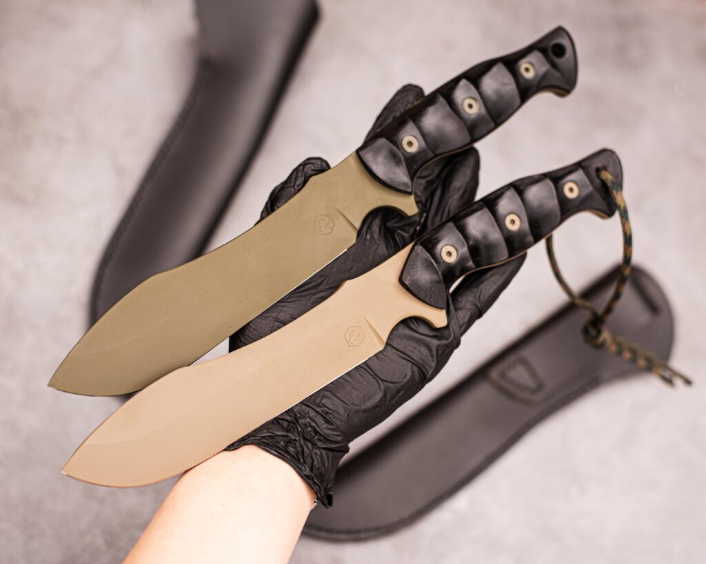 80CrV2 high carbon steel in cerakote coating. Black G10 handles and leather sheaths.