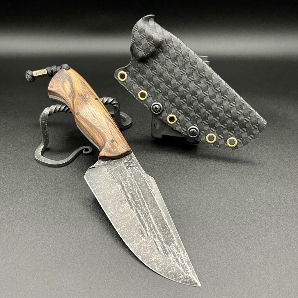 80crv2 high carbon steel. The handle is carved from zebra wood with black g10 pins & a brass eyelet. Sheathed in Basketweave Kydex with an adjustable carry and lockable combat loop