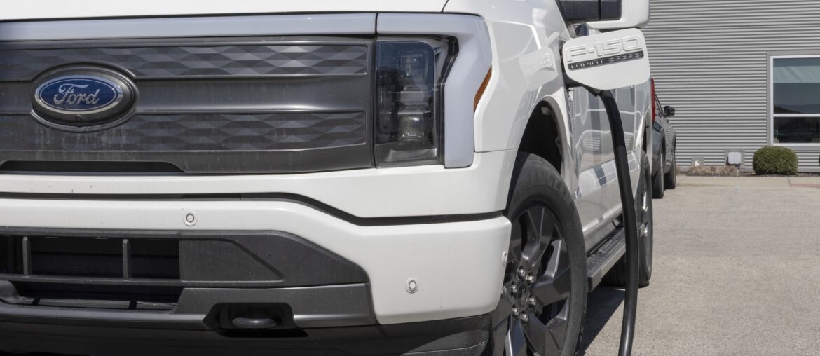 A white Ford F-150 Lightning electric truck charging at a station.